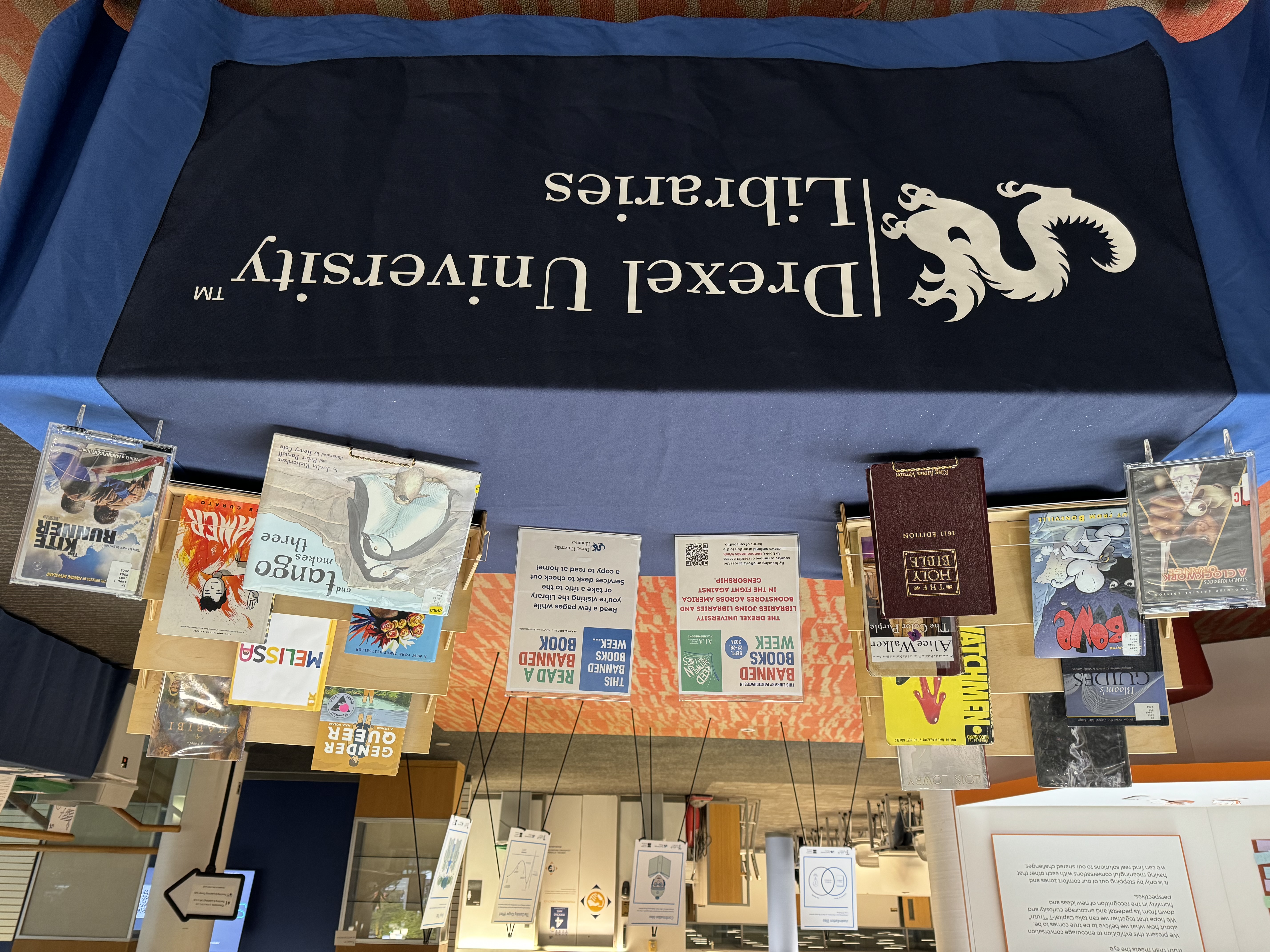 Drexel Libraries' 2024 Banned Books display featuring ALA graphics and titles on blue tablecloth with Libraries logo.